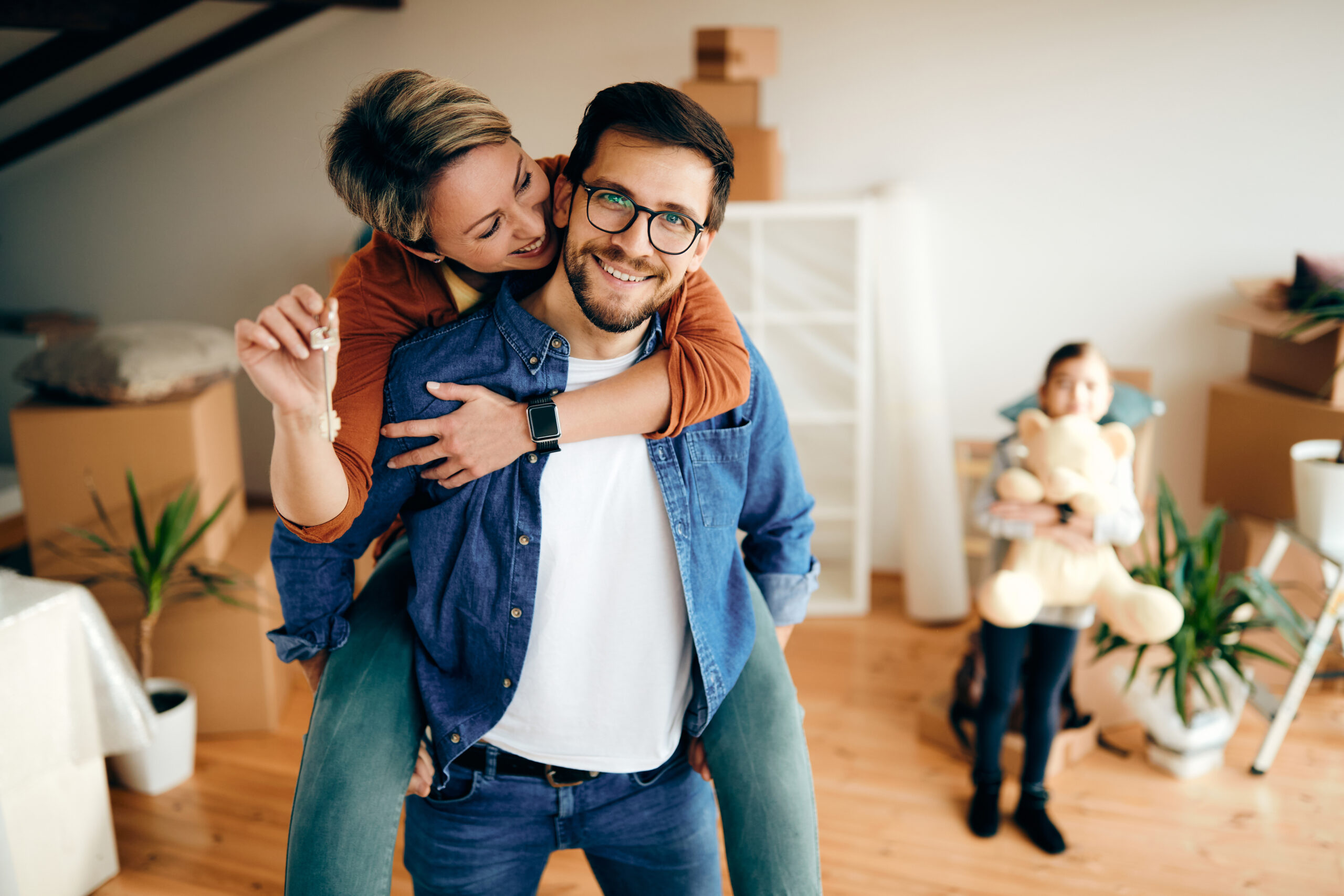 Happy mid adult couple having fun while relocating into a new house. Their daughter is in the background.
